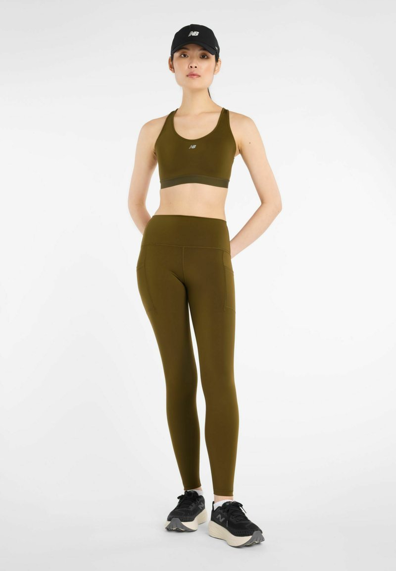 Olivgrön sport-bh och högmidjade leggings i stretchigt material, kombinerade med svarta sneakers och en matchande keps.