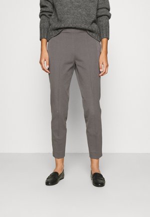 Person wearing gray tailored ankle-length pants, dark gray knit sweater, and black loafers standing against a white background.