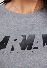 Sudadera de algodón gris con un diseño de logo negro audaz. La tipografía es grande y texturizada, con un cuello redondo y mangas cortas.