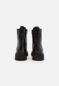 Černé kožené kotníkové boty s hladkým povrchem, bočním zipem a robustními gumovými podrážkami. Prošití zvýrazňuje design.