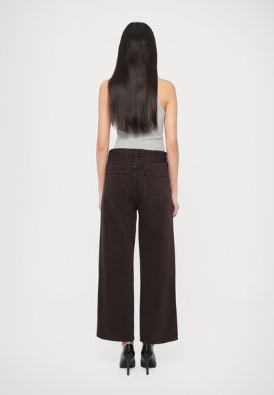 Sötétbarna, széles szárú farmernadrág, magasított derékkal, öt zsebbel és látható varrással, világosszürke ujjatlan felsővel párosítva.