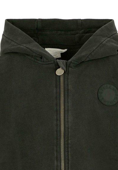 Giacca cappuccio grigia scura con zip frontale, caratterizzata da una patch rotonda con logo sul lato sinistro e una texture del tessuto liscia.