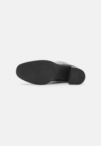 Black heeled shoe featuring a smooth upper, rounded toe, and textured rubber sole with a subtle pattern for grip and stability.