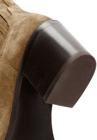 Suede ankle boot in light brown with a block heel, featuring a smooth black finish and subtle stitching details on the upper.