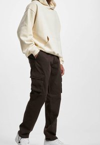 Beige capuchon sweatshirt met een voorzak, gecombineerd met donkerbruine cargobroeken met zijzakken. Model draagt witte sneakers.