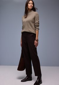 Pull beige en maille avec un col montant et une texture côtelée, associé à un pantalon marron foncé et des bottines noires arrivant à la cheville.