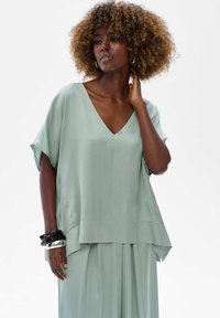 Jasnozielona, luźna bluzka z dekoltem w serek i krótkimi rękawami. Wykonana z gładkiego materiału, z warstwowym dołem i swobodnym krojem.