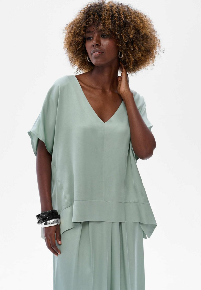 Jasnozielona, luźna bluzka z dekoltem w serek i krótkimi rękawami. Wykonana z gładkiego materiału, z warstwowym dołem i swobodnym krojem.
