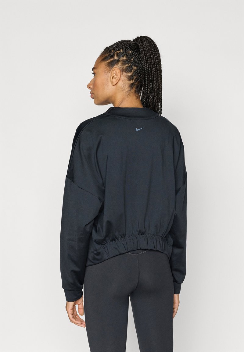 Zwarte Nike-trui met een cropped design, elastische tailleband en lange mouwen. Voorzien van een klein logo op de achterkant. Gladde textuur.