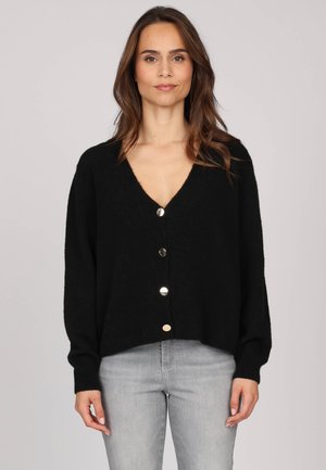 Cardigan noir en tricot avec un col en V, cinq grands boutons argentés sur le devant et des épaules tombantes. Texture légère, coupe décontractée.