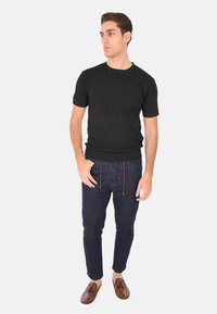 Maglietta nera a maniche corte in maglia ribbed abbinata a pantaloni in denim scuri con coulisse e scarpe stringate marroni. Design semplice e aderente.