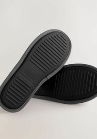 Schwarze Gummisohle mit horizontalen und vertikalen Rillen. Verfügt über eine strukturierte Oberfläche und eine geprägte Größenangabe, die für Langlebigkeit ausgelegt ist.