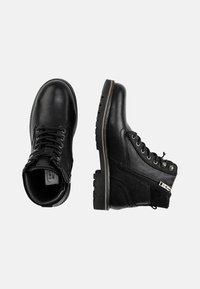 Botas de tobillo de cuero negro con un acabado texturizado, diseño de cordones, cremallera lateral y suelas robustas. Costuras reforzadas y ojales de metal.