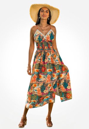 Woman wearing a colorful, patterned sundress, wide-brim straw hat, and brown wedge sandals, standing with one hand holding the dress hem.