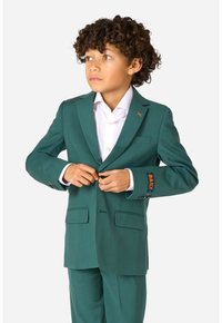 Completo verde con un design su misura, dotato di due tasche frontali, una camicia bianca sotto e un dettaglio decorativo sulla manica.