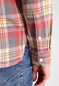 Camicia a quadri rossi e grigi con accenti gialli, polsini abbottonati, realizzata in tessuto intrecciato, che mostra un classico motivo a scacchi e una vestibilità su misura.