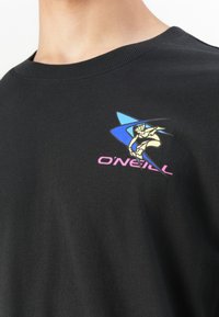 Camisa negra con un logo colorido de O'Neill que muestra un surfista estilizado y una ola azul, llevada por una persona con el cuello y la barbilla visibles.