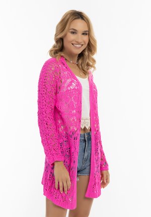Rosa, öppet stickad cardigan med långa ärmar och lös passform. Bärs över en vit crop top och denimshorts, med intrikata spetsliknande mönster.