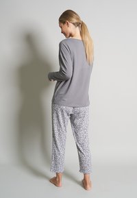 Gray long-sleeve top paired with gray leopard-print pajama pants. Soft fabric, relaxed fit, ankle-length with a subtle pattern in shades of gray.