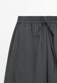 Dark gray pants with an elastic waistband and drawstring, showing side pockets and smooth fabric texture.