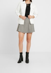 Vit denimjacka över en svart topp, kombinerad med en svart och vit rutig kjol och svarta ankelstövlar med en kraftig klack.