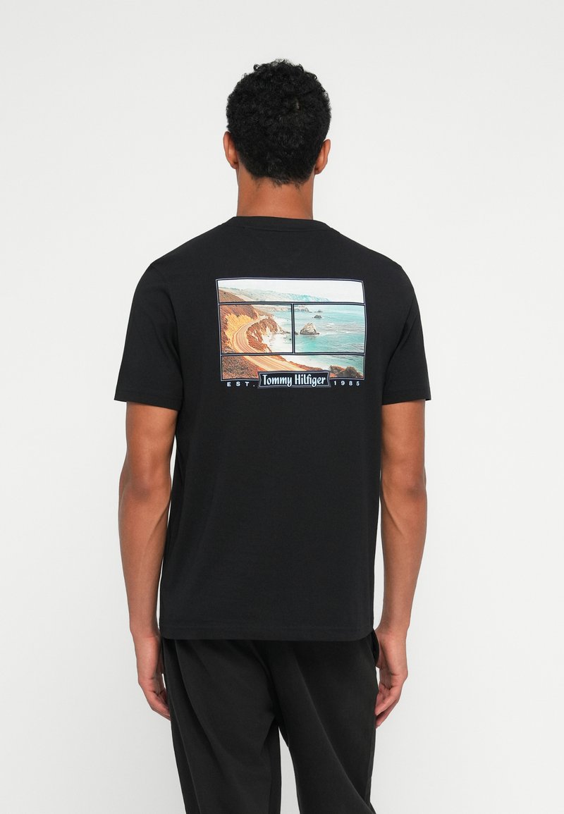 Sort bomulds t-shirt med et grafisk motiv af to kystlandskabsbilleder på ryggen, med "Tommy Hilfiger" tekst og etableringsdato.