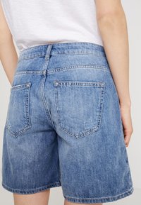 Vaaleansiniset farkkushortsit, joissa on keskipitkä vyötärö, kaksi takataskua ja rento malli. Langantiehystyksellä taskujen ja helman ympärillä.