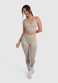 Beige geripptes Sport-BH und hochtaillierte Leggings mit einem Cut-Out-Design. Das Outfit wird mit weißen Sneakers vor einem neutralen Hintergrund kombiniert.