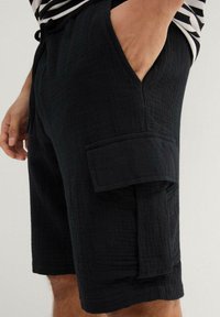 Pantaloni cargo neri realizzati in tessuto testurizzato, con una tasca laterale e una vita elastica con cordino per una vestibilità regolabile.