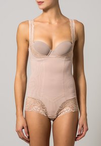 Nude bodysuit with lace trim, adjustable straps, padded cups, smooth texture, and shaping panels for support. Features decorative floral accents.