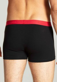 Zwarte boxershorts met een rode tailleband waarop het merk "CALIDA" in bijpassende rode letters is afgebeeld, gemaakt van een soepele, rekbare stof.
