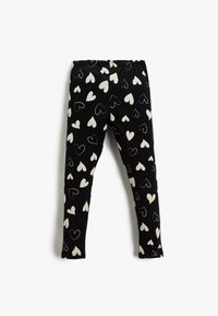Czarne legginsy z wzorem białych serc, wykonane z miękkiego materiału z elastycznym pasem dla wygody. Slim fit.