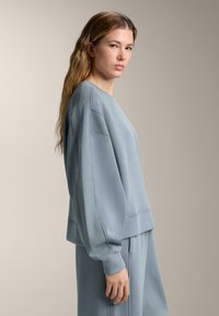 Ljusblå sweatshirt med ribbad textur, raglanärmar och en avslappnad passform. Matchad med byxor av samma färg, vilket skapar en sammanhängande look.