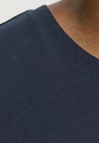 Tejido de algodón azul marino con una textura suave y un cuello redondo acanalado. La vista en primer plano enfatiza las costuras y la profundidad del color.