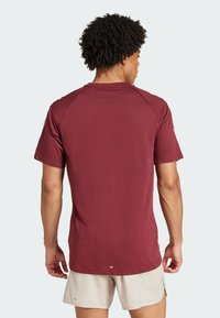 Camiseta burdeos de manga corta, textura lisa, cuello redondeado y detalles de costuras en las mangas raglán, combinada con pantalones cortos beige.