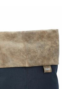 Borsa in tela con un cappello in pelle marrone ripiegabile, con cuciture visibili. Base in tessuto blu scuro con un piccolo etichetta del marchio sul lato.