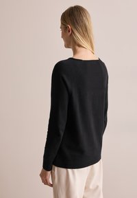 Schwarzer Strickpullover mit einem runden Halsausschnitt, Raglanärmeln und einer lockeren Passform. Glatte Textur und minimale Designmerkmale.