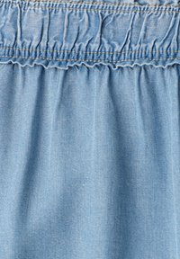 Tissu en denim bleu clair avec fronces élastiques et une couture cousue créant une texture froncée près du bord supérieur.