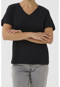 Svart V-ringad t-shirt med korta ärmar, tillverkad av mjukt tyg. Bärs med ljusgrå jeans och framhäver en avslappnad passform och enkel design.