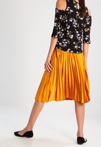 Czarny kwiatowy top bez ramiączek z krótkimi rękawami; plisowana żółta spódnica; czarne płaskie buty. Detal w kształcie łezki na plecach topu.