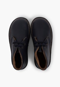 Granatowe skórzane buty z miękkim, brązowym futrem w środku, z niskim krojem, dwoma otworami na sznurowadła i kontrastowym przeszyciem wzdłuż podeszwy.