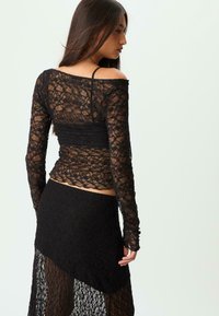 Sort blonde top med lange ærmer og off-the-shoulder design, parret med en matchende sort blonde nederdel med en asymmetrisk kant.