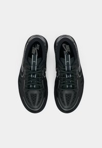 Par crnih Nike Air tenisica s reflektirajućim detaljima, vezice su vezane, prikazane iz gornjeg pogleda na bijeloj pozadini.