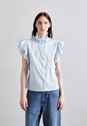 Light blue blouse with ruffled short sleeves, collar, and button front. Worn with loose-fitting denim jeans against a neutral background.