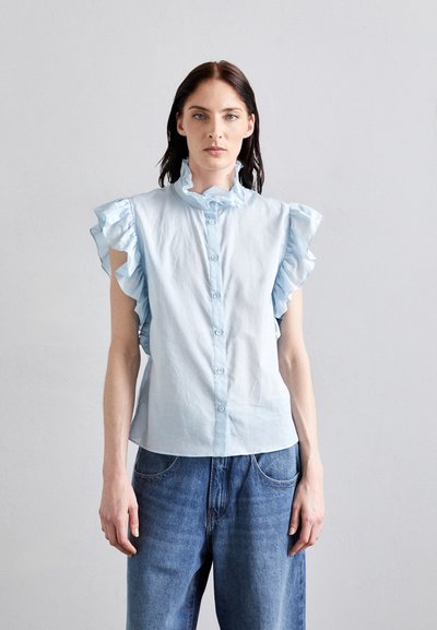 Bluză de culoare albastru deschis, cu mâneci scurte volănașe, guler și închidere cu nasturi. Purtați cu blugi din denim cu croială lejeră, pe un fundal neutru.