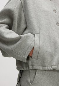 Grijze sweatshirt met een ontspannen pasvorm, voorzien van een knoopsluiting, geribde manchetten, zijzakken en een verstelbare trekkoord aan de onderrand.