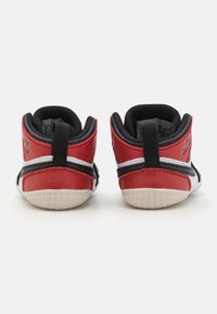 Røde og svarte sneakers med overdel i lær og mesh, med hvite striper, teksturerte hælinnsatser og gummisåle med rutenettmønster.