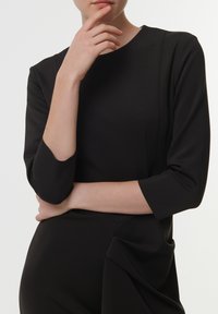 Vestido negro con escote redondo, mangas tres cuartos y detalle de drapeado asimétrico en la cintura. Tela suave y texturizada.