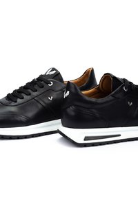 Zwarte leren sneakers met een witte rubberen zool. Kenmerken zijn onder andere ronde veters, een logo op de tong en subtiele stikseldetails.