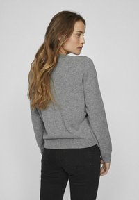 Pilkas megztinis su ilgomis rankovėmis, apvaliu iškirpimu ir srieginių apdaila. Minkšta tekstūra; dėvimas su juodomis džinsinėmis kelnėmis.